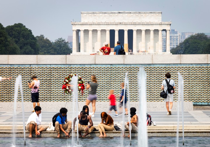 Visitantes del Monumento a los Caídos en la II Guerra Mundial se refrescan en la piscina del monumento durante un día caluroso y húmedo en Washington DC, Estados Unidos. EFE/EPA/JIM LO SCALZO